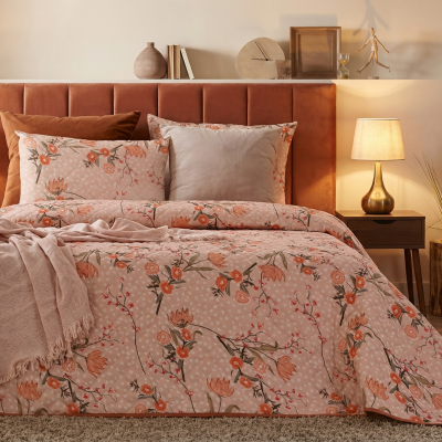 Cama com edredão floral rosa e cabeceira castanha com candeeiros dourados em mesas de cabeceira.
