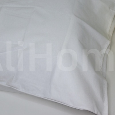 Almofada branca lisa colocada numa mesa com vaso dourado e plantas verdes