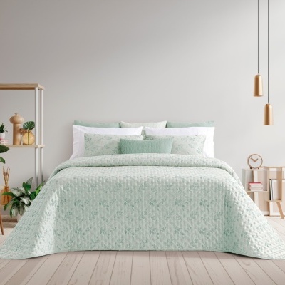 Cama de casal com colcha verde clara e padrão floral numa decoração minimalista com plantas e lâmpadas pendentes