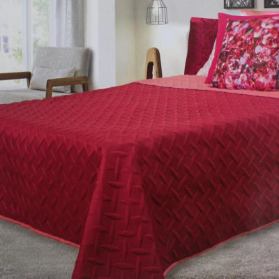 colcha vermelha com almofadas decorativas em cama de ambiente interior com poltrona e mesa lateral