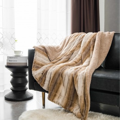 Manta felpuda castanha sobre sofá preto ao lado de mesa com livros e chávena