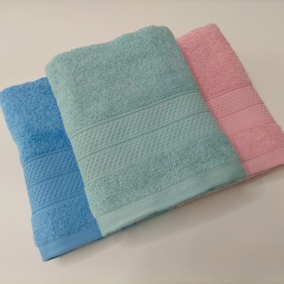 Três toalhas de banho azul, verde água e rosa com texturas distintas empilhadas numa superfície clara