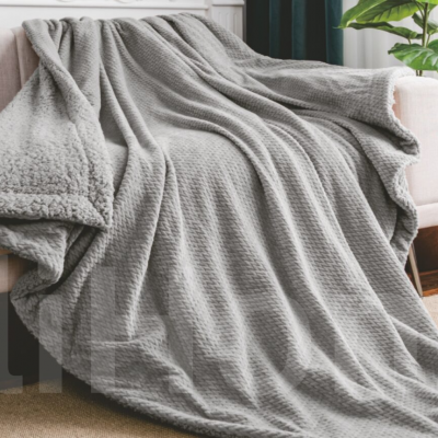 Cobertor cinzento texturizado sobre sofá claro em interior com plantas