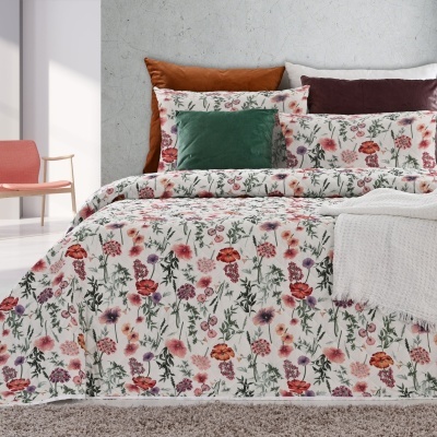 Jogo de cama floral com várias almofadas coloridas numa cama, cadeira e mesa lateral no ambiente