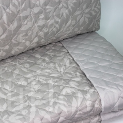 Colchão ou almofada bege com padrão floral e superfície cinza clara ao lado de planta verde