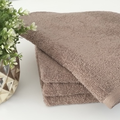 Toalha castanha felpuda dobrada ao lado de vaso dourado com planta verde