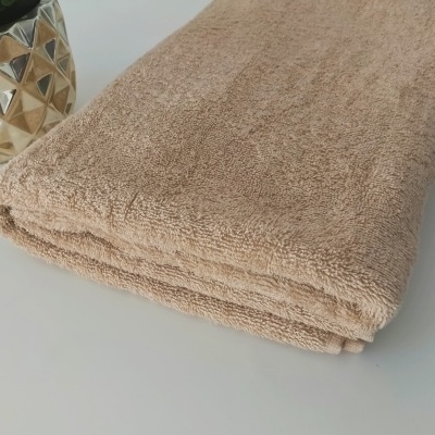 Toalha bege felpuda dobrada com vaso dourado ao fundo