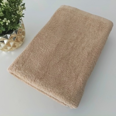 Toalha castanha clara dobrada sobre uma superfície branca com planta em vaso dourado