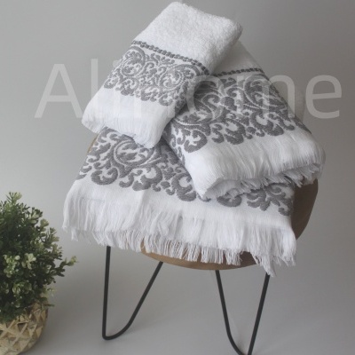 Toalhas brancas com padrão cinza decorativo sobre cadeira de madeira com vaso de planta ao lado