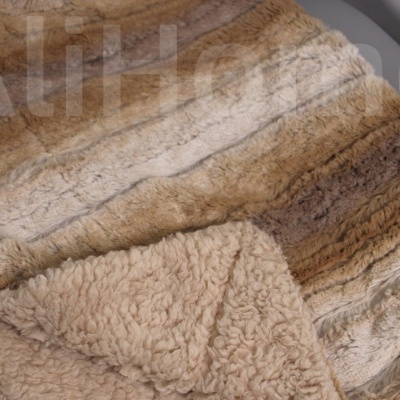 Manta peluda em tons castanhos e bege dobrada sobre superfície cinzenta