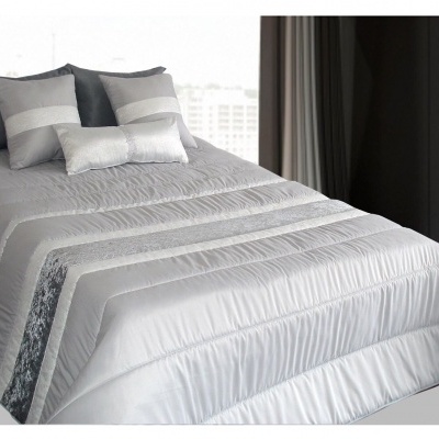 Colcha prateada e cinza com almofadas cinzentas numa cama junto a janela