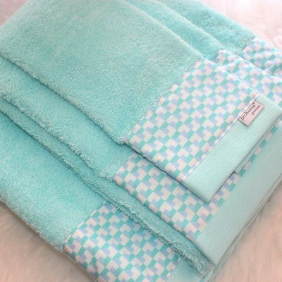 Conjunto de toalhas azul-turquesa com bordado decorativo em superfície rosa