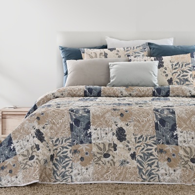 Cama com edredão floral em tons azuis e bege, com almofadas decorativas e planta ao lado