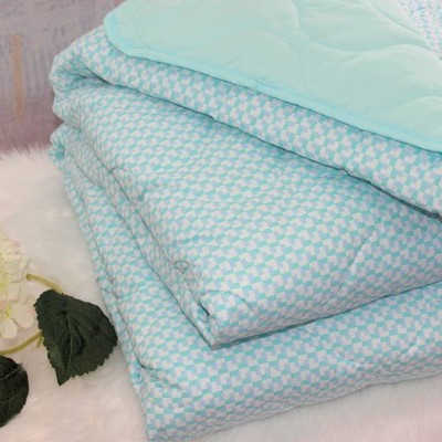 Edredão azul claro com padrão geométrico branco e verso azul liso sobre superfície branca com flor decorativa