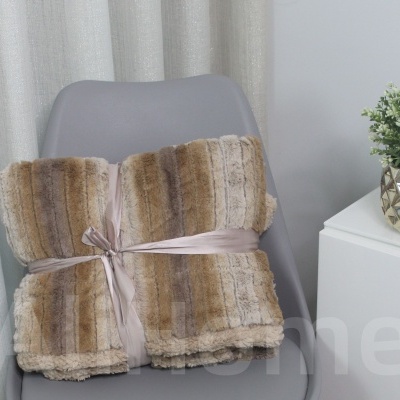 Manta de pelo sintético em tons castanhos sobre cadeira cinza junto a mesa branca com planta