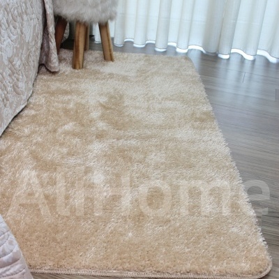 Tapete bege peludo retangular sobre chão de madeira clara junto a banco peludo e planta em vaso dourado