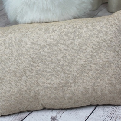 Almofada bege com padrão geométrico sobre chão de madeira junto a almofada branca felpuda