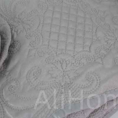 Colcha cinzenta clara com padrão matelassê e bordado detalhado