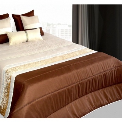 Cama com edredão castanho e almofadas castanhas, bege e brancas, em quarto interior