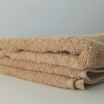 Toalha de banho bege dobrada sobre mesa branca