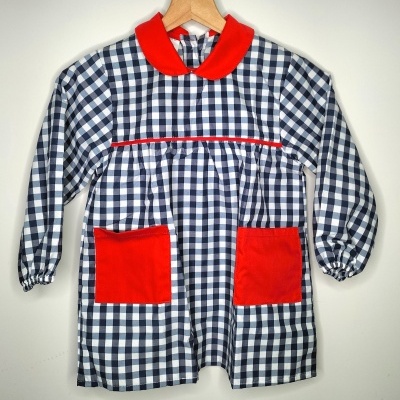 Vestido xadrez azul e branco com gola e bolsos vermelhos, pendurado num cabide