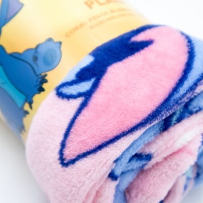 Toalha coral fleece cor de rosa, azul e lilás enrolada com rótulo amarelo e figura azul