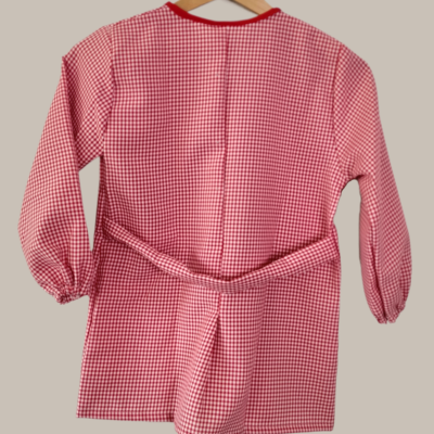 Casaco infantil vermelho e branco de manga comprida com padrão vichy, pendurado num cabide.