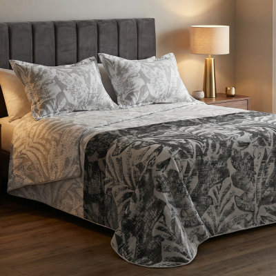 Cama de casal com roupa de cama em padrão botânico cinza e branco, cabeceira cinzenta, mesas de cabeceira em madeira e candeeiros dourados.