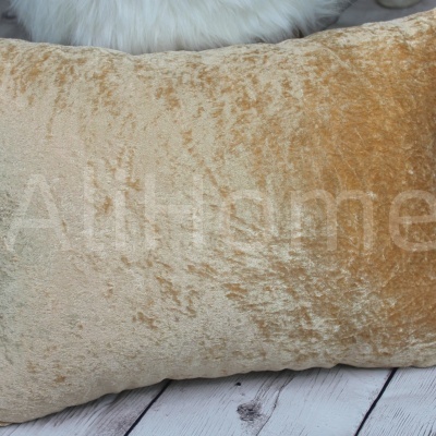 Travesseiro dourado aveludado rectangular sobre chão de madeira