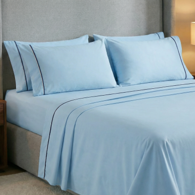 Cama com conjunto de roupa de cama azul claro com riscas azuis escuras, em quarto com mesas de cabeceira e candeeiros.