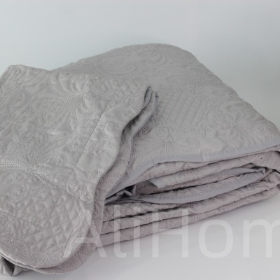 Colcha cinzenta texturizada dobrada ao lado de planta em jarra dourada