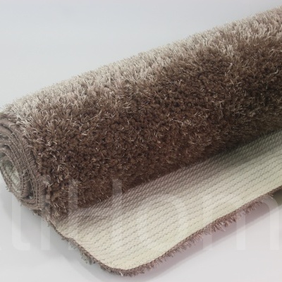 Tapete castanho felpudo em rolo ao lado de vaso dourado com planta