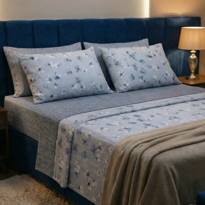 Cama com roupa de cama azul e cinza floral e cabeceira azul escura ao lado de duas mesas de cabeceira com candeeiros