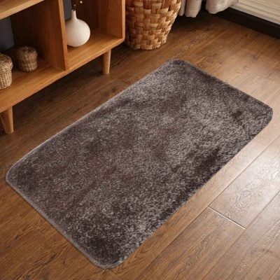 Tapete cinza escuro felpudo sobre chão de madeira com móvel e cesto ao fundo