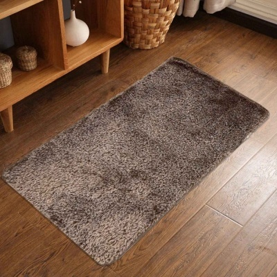 Tapete cinzento felpudo sobre chão de madeira junto a estante e cesta