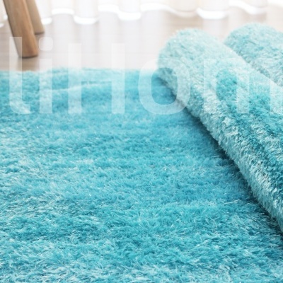 Tapete felpudo azul turquesa parcialmente enrolado sobre chão claro