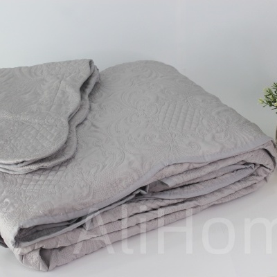 Colcha e almofada cinzentas com padrão texturizado e planta em vaso dourado