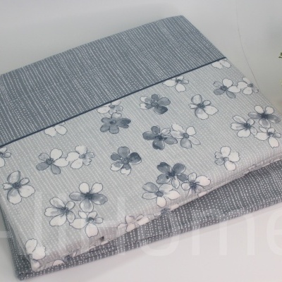 Cobertor ou capa cinza com padrão floral e listrado ao lado de vaso dourado com planta