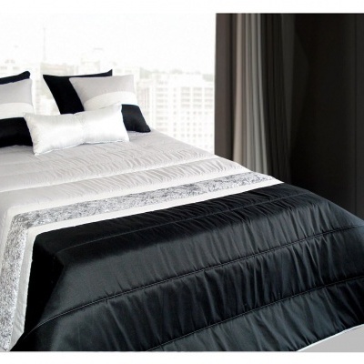 Colcha de cama branca, cinza e preta com almofadas num quarto claro