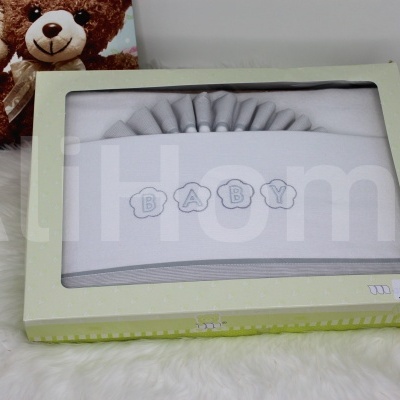 Manta para bebé cinzenta com palavra BABY embalada em caixa verde clara sobre superfície branca felpuda