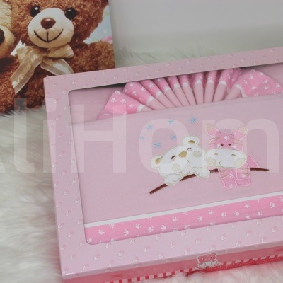 Caixa de presente rosa com ursinhos bordados, tecido rosa às bolinhas e leque decorativo em fundo branco macio com dois ursos de pelúcia ao fundo