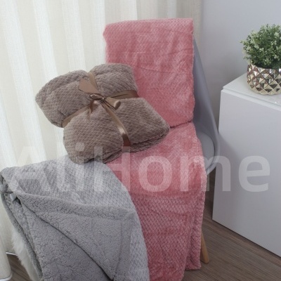 Três mantas macias emposite numa cadeira e ao lado, com cortinas e móvel decorativo