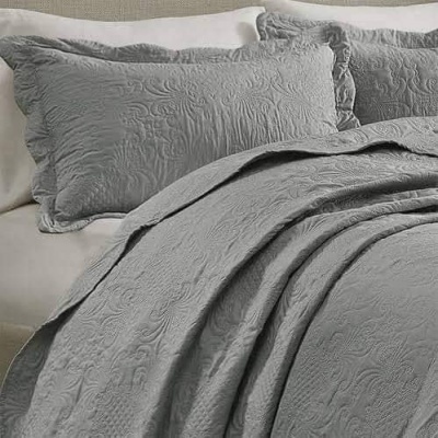 Conjunto de cama cinzento com padrão texturizado e almofadas, sobre lençol branco.