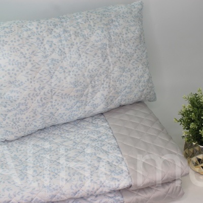 Almofada e edredão de padrão floral com vaso dourado e planta