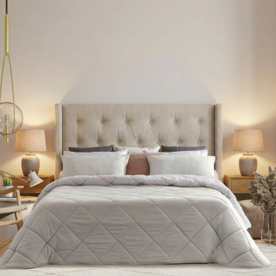 Cama grande com cabeceira estofada bege e edredão cinzento em quarto moderno e luminoso