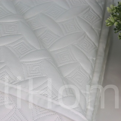 Colchão branco com padrão em relevo ao lado de planta em vaso dourado