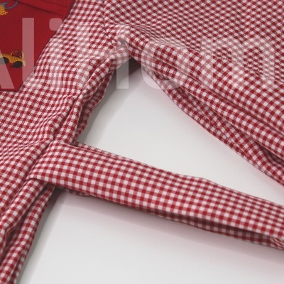 Peça de roupa infantil xadrez vermelho e branco com cinto, sobre superfície branca
