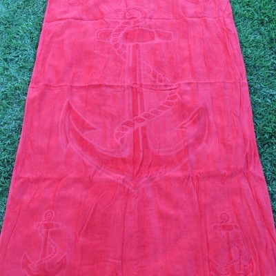 Toalha de banho vermelha com âncoras em relevo e texto ALiHome sobre relva