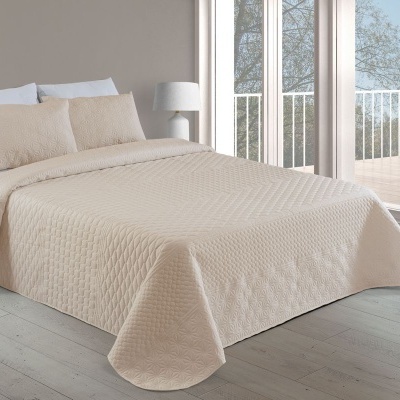 Cama de casal com colcha bege matelassada e almofadas, junto a janela grande