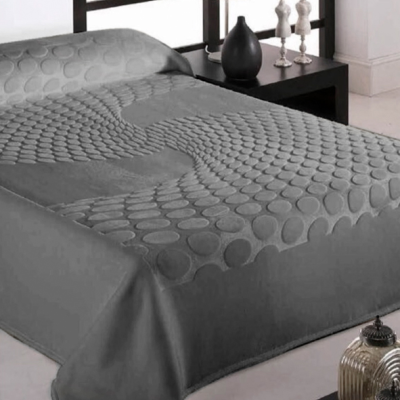 Cobre-leito cinzento com padrão circular em relevo sobre cama com mesa de cabeceira e candeeiro